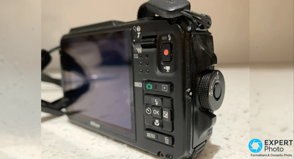Nikon Coolpix AW110 vu 3/4 arrière droit, boutons SCENE, OK, MENU visibles, molette de modes sur le flanc