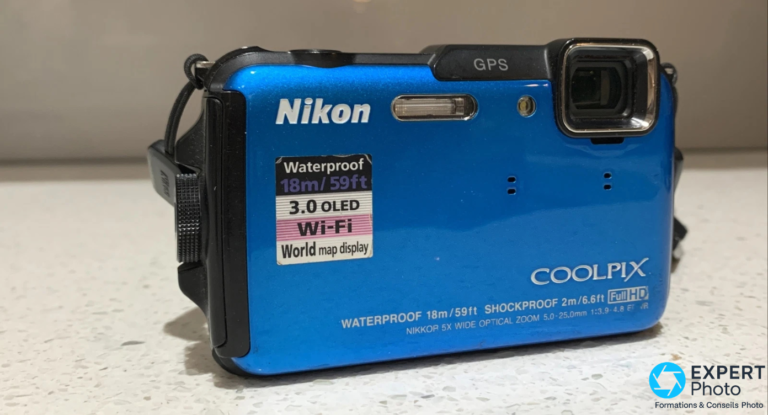 Nikon Coolpix AW110 avis: compact baroudeur d’occasion, pas un étanche universel Nikon Coolpix AW110 bleu posé sur surface granit, face avant avec vignette spécifications incrustée : Waterproof 18m, Wi-Fi, 3.0 OLED