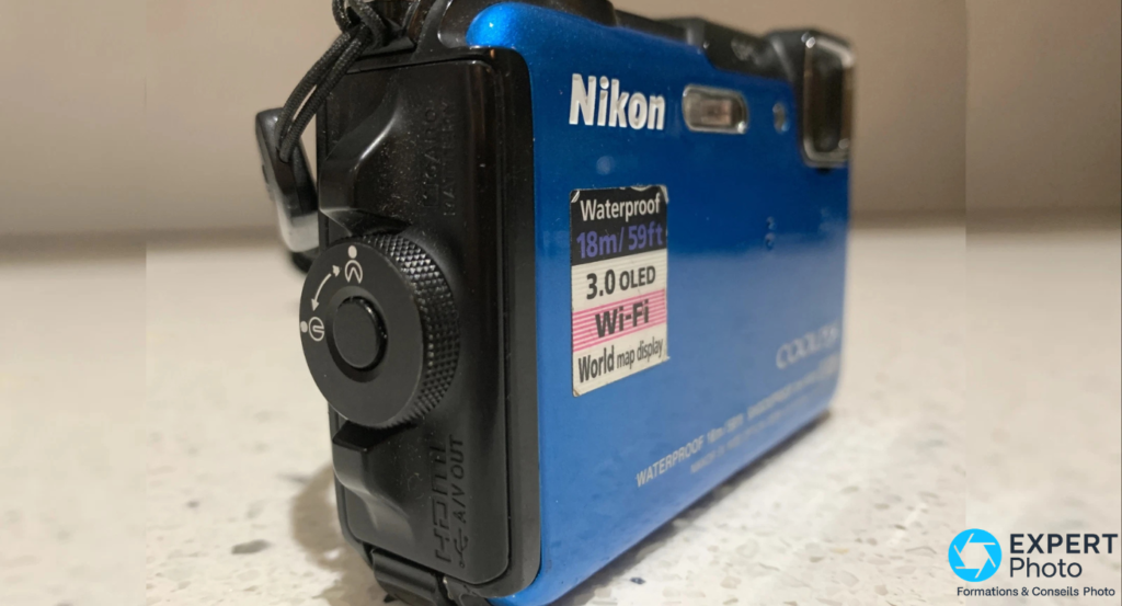 Profil droit du Nikon Coolpix AW110 bleu, trappe connectiques A/V, molette de mode et sticker Waterproof Wi-Fi incrusté