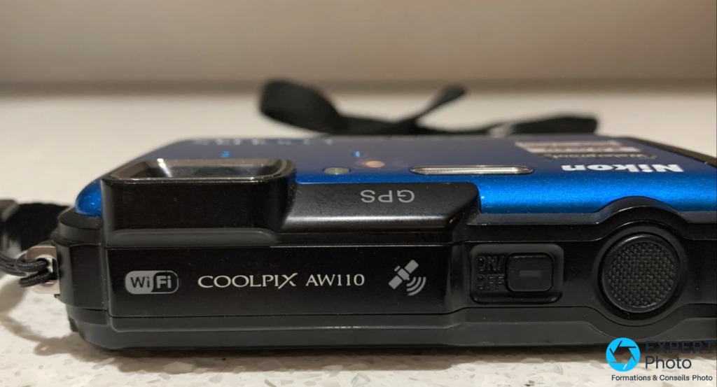 Tranche supérieure du Nikon Coolpix AW110 avec inscription COOLPIX AW110, logos Wi-Fi et GPS, bouton ON/OFF visible
