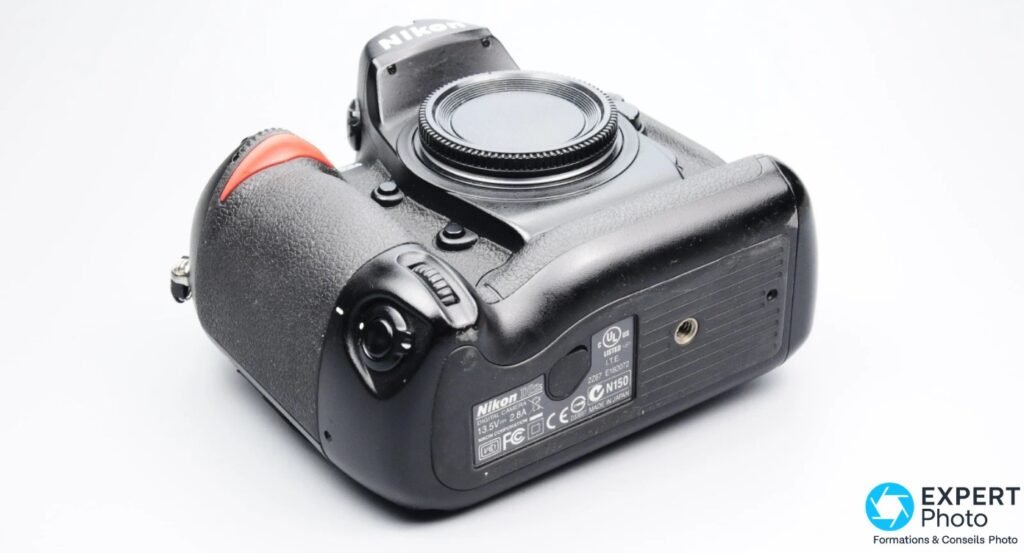 Nikon D2Hs, vue semelle 3/4 arrière, étiquette constructeur avec mention Made in Japan et certifications, filetage trépied, fond blanc