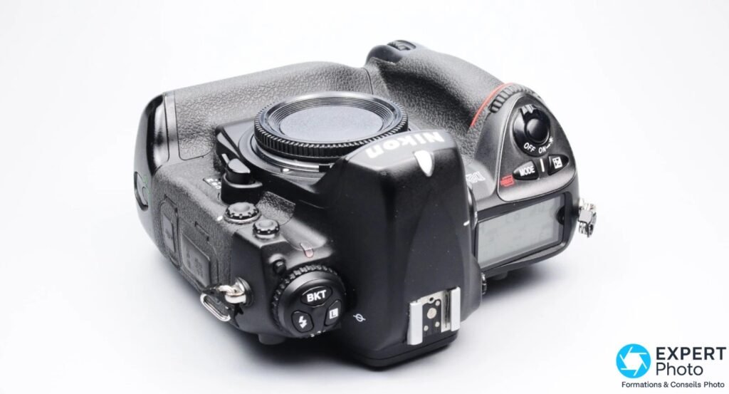 Nikon D2Hs noir, vue plongeante de dessus, cache monture, bouton BKT, molette OFF/ON et griffe flash visibles, fond blanc