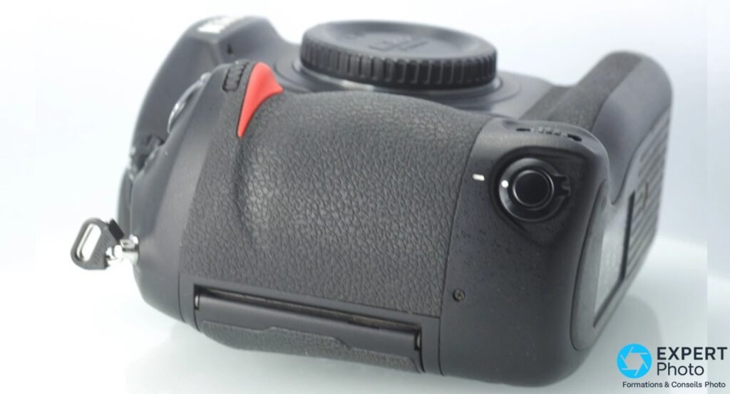 Profil gauche Nikon D3, grip texturé noir, repère rouge de monture, anneau sangle métal, trappe inférieure