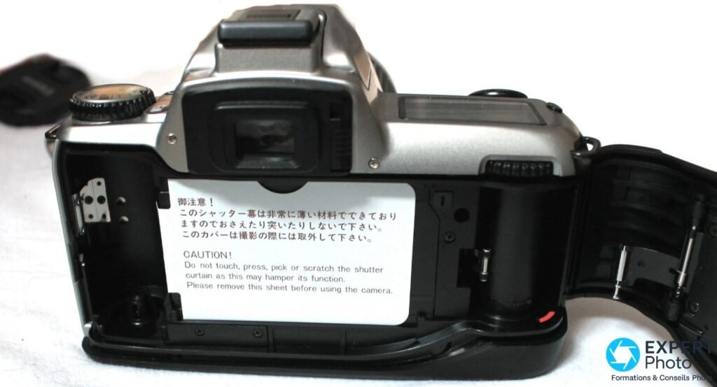Nikon F65 trappe arriere ouverte, compartiment film avec fiche avertissement Nikon bilingue japonais-anglais, fond blanc.