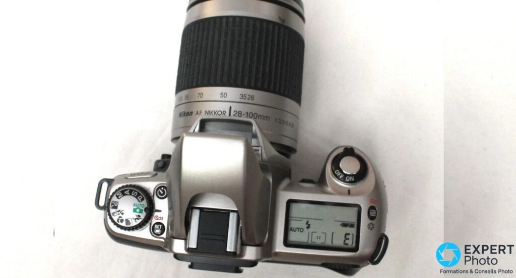Dessus du Nikon F65 en plongee : molette de modes, objectif Nikon AF NIKKOR 28-100 mm, afficheur LCD affichant AUTO et E.