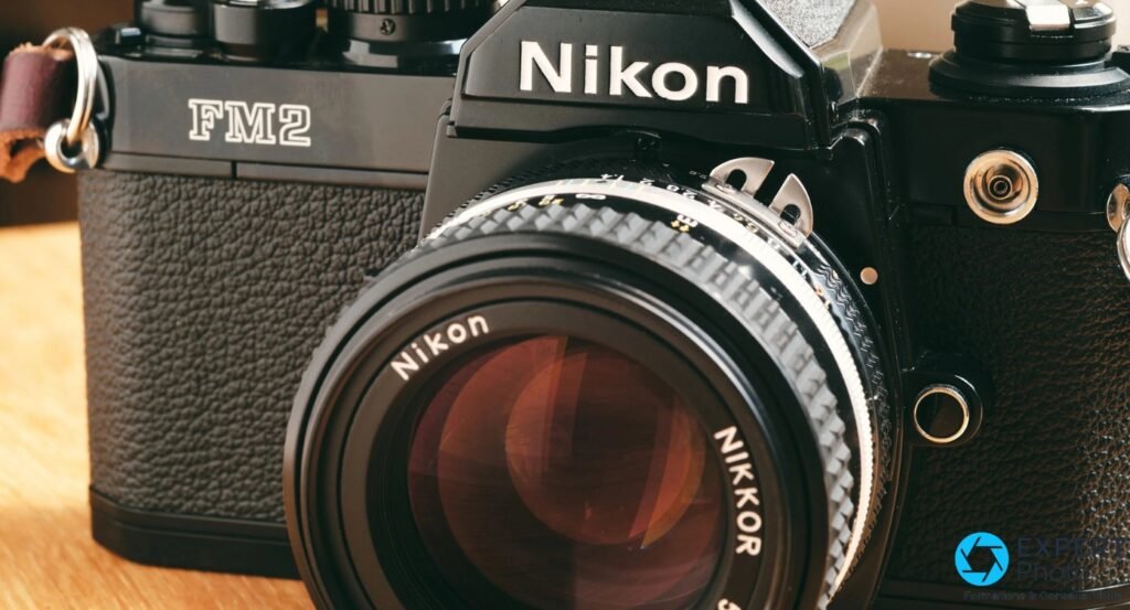 Gros plan sur l'objectif Nikon Nikkor monté sur un Nikon FM2n noir posé sur une surface en bois, bague de mise au point visible