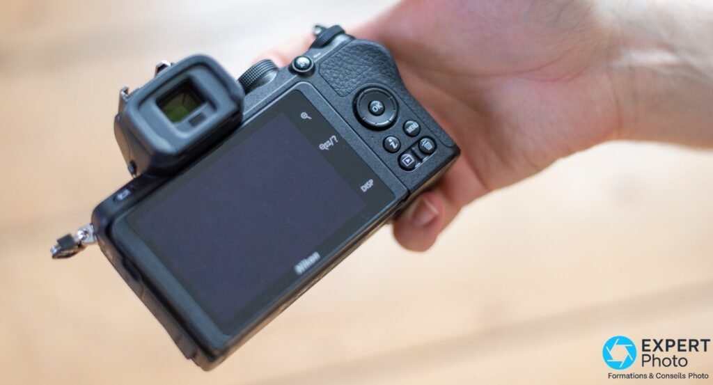 Nikon Z50 vu de dos, écran tactile éteint, boutons OK, MENU et molette visibles, viseur OLED à gauche, tenu en main 