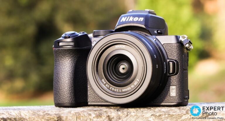 Nikon Z50 noir de face, Nikkor Z DX 16-50mm f/3.5-6.3 VR monté, logo Z50 bas droite, posé sur surface pierre, fond vert flou