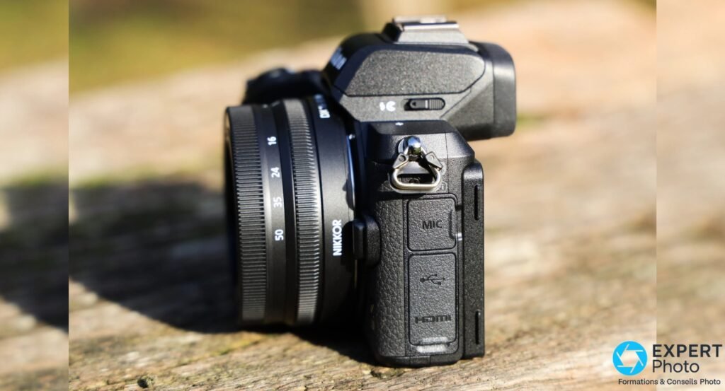 Nikon Z50 profil gauche, capots ouverts révélant les connecteurs MIC, USB Micro-B et HDMI, objectif Nikkor DX monté, posé en extérieur