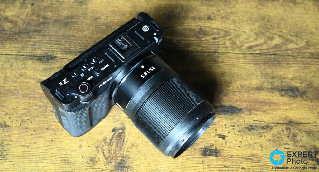 Nikon ZR noir posé à plat sur bois, vu de dessus, objectif Z 35/1.8 S monté, boutons PHOTO VIDEO MODE visibles 