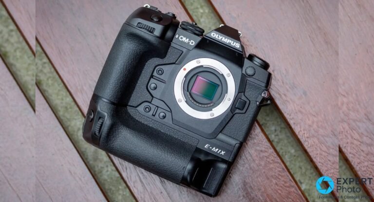 Olympus OM-D E-M1X boîtier nu de face sur surface bois, monture ouverte avec capteur Micro 4/3 visible, inscription E-M1X sur le grip