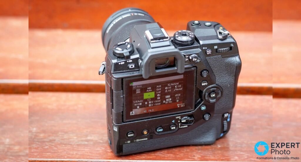 Olympus OM-D E-M1X vu de dos, écran LCD allumé affichant un menu de réglages AF et stabilisation, touches INFO, OK et Fn visibles