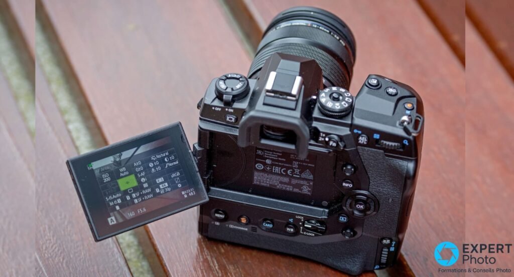 Olympus OM-D E-M1X vu de dos, écran LCD basculant ouvert affichant un menu de réglages, viseur EVF et touches du dos visibles