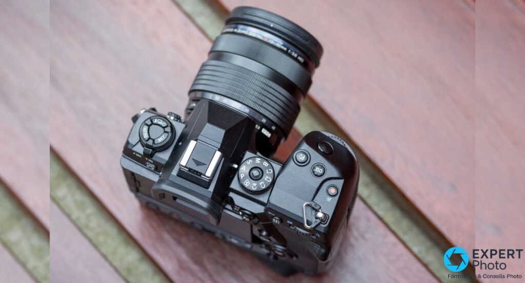 Olympus OM-D E-M1X vu du dessus, molette de modes P/A/S/M, touches ISO et Fn, et objectif zoom monté visibles