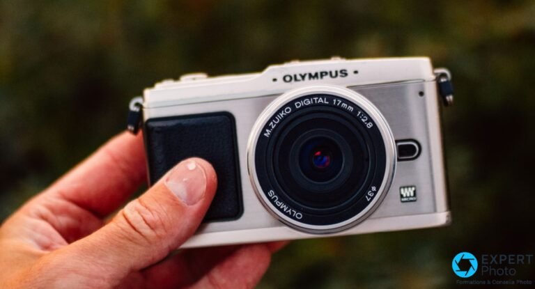 Olympus Pen E-P1 blanc tenu en main, face avant, objectif M.Zuiko Digital 17mm f/2.8 monté, fond vert flou