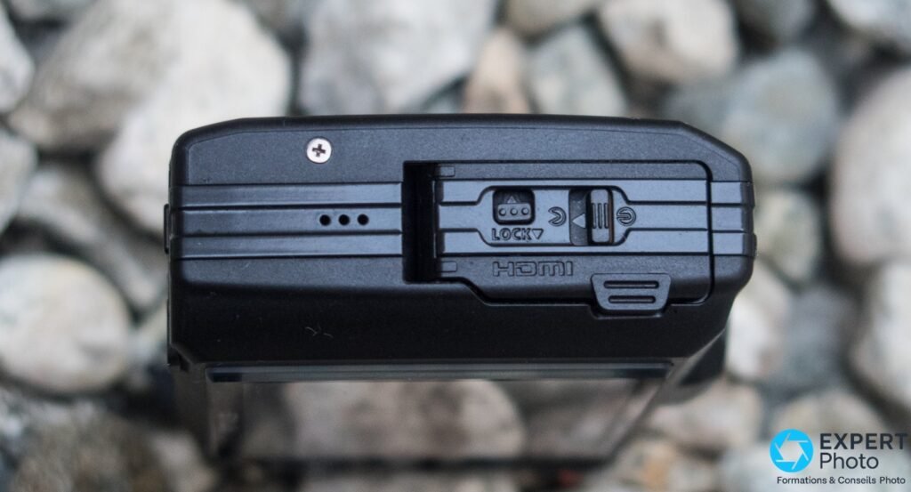 Côté gauche de l'Olympus Tough TG-3, trappe étanche fermée avec verrou LOCK et marquage HDMI visible, fond de galets