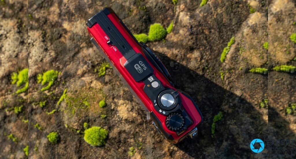 Dessus Olympus Tough TG-6 rouge sur roche mosseuse, capot GPS Wi-Fi gravé, déclencheur métal et bague zoom W/T visibles