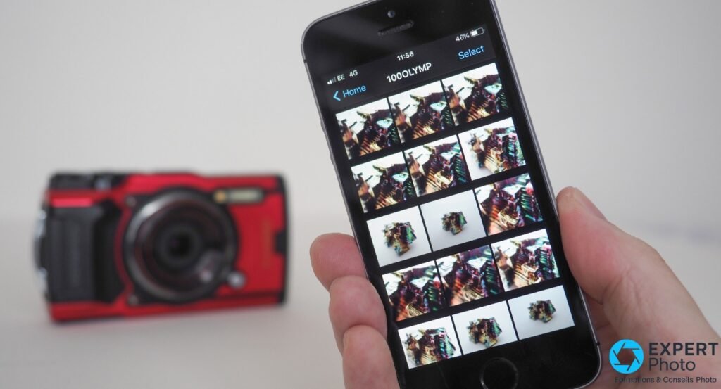 Main tenant un smartphone iOS, dossier 100OLYMP ouvert avec vignettes photos, Olympus Tough TG-6 rouge flou en arrière-plan
