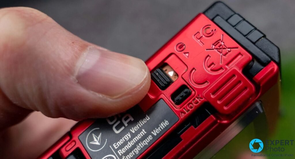 Fond du TG-6 rouge, trappe batterie ouverte, verrou ALOCK, certifications FC CE, batterie partiellement visible en main