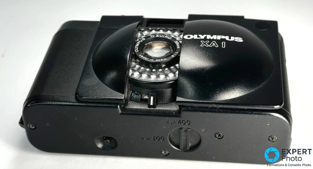 Olympus XA1 en vue plongée, molette ISO avec graduations ASA 100 et ASA 400, objectif D.Zuiko 35mm f/4, flash externe