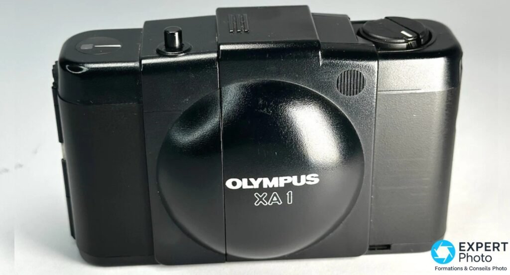 Olympus XA1 noir face avant, clapet circulaire fermé avec inscription OLYMPUS XA1, flash externe sur griffe