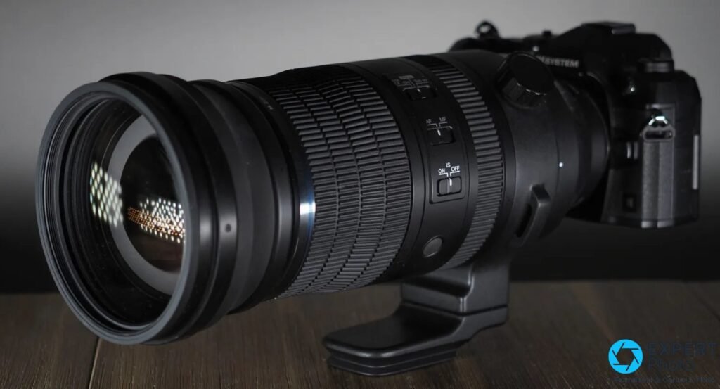 OM System M.Zuiko 150-600mm de profil sur bois, lentille avant sans cache, commutateurs AF/MF et IS ON/OFF lisibles