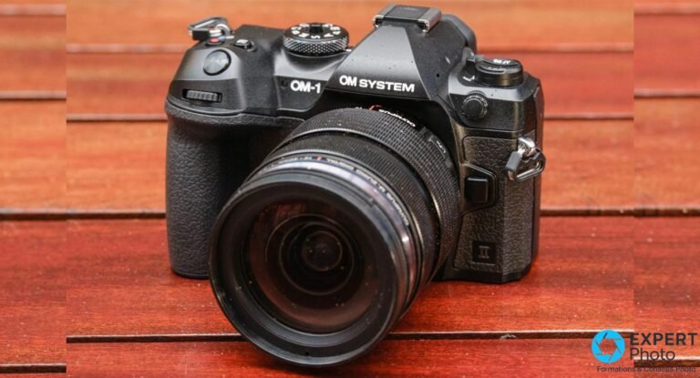 OM System OM-1 Mark II noir face avant, objectif zoom monté, posé sur des lattes de bois rouge