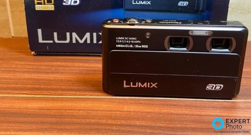 Panasonic DMC-3D1 noir face avant sur bois, boîte bleue HD 3D Lumix en arrière-plan, traces d'usure légères