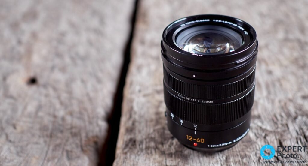 Objectif Panasonic Leica DG Vario-Elmarit 12-60mm f/2.8-4 posé sur bois brut, inscriptions 12-60 et LEICA DG VARIO-ELMARIT lisibles