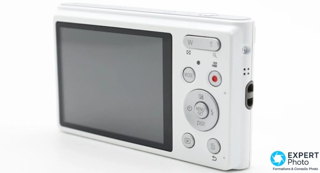 Panasonic Lumix DMC-XS1 vu de trois quarts arrière, écran éteint, boutons MODE, MENU/SET, DISP. et déclencheur vidéo rouge visibles