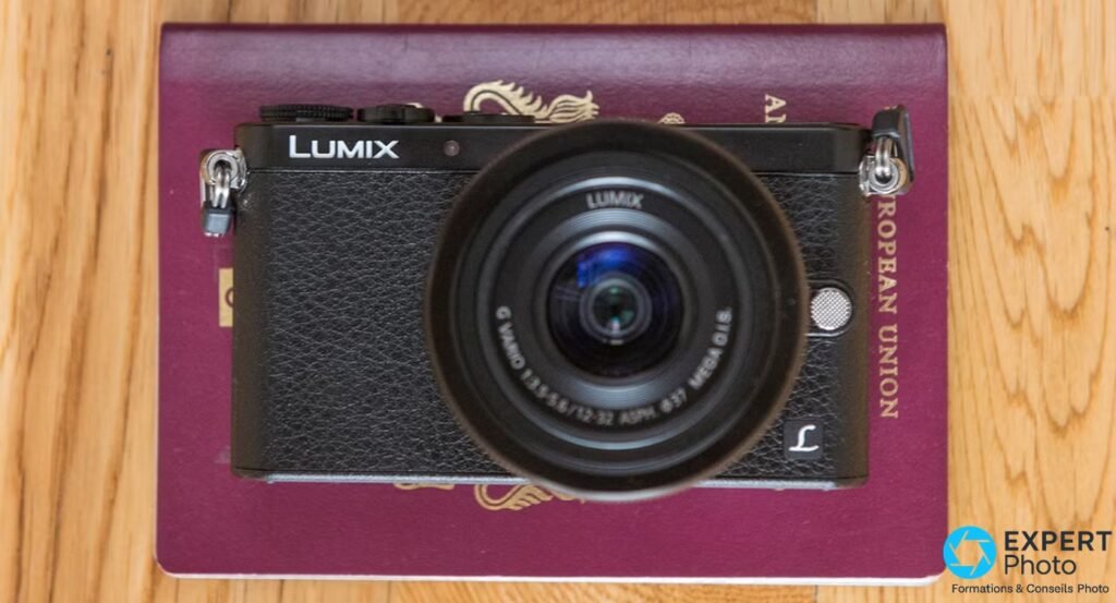Panasonic Lumix GM1 noir avec objectif 12-32 mm posé sur un passeport bordeaux, vue de dessus sur fond parquet