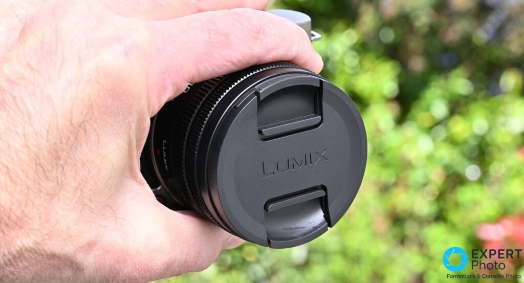 Objectif Lumix S 18-40mm seul avec bouchon avant Lumix posé, bagues de zoom et mise au point visibles, fond vert flou