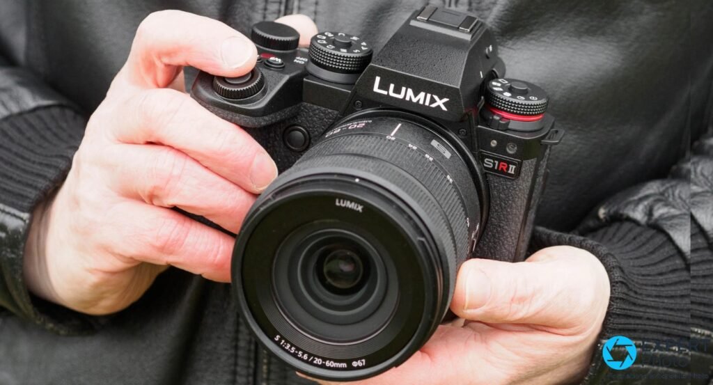 Panasonic Lumix S1R II tenu en main, face avant, objectif Lumix S 20-60 mm f/3.5-5.6 monté, marquage S1R II lisible 