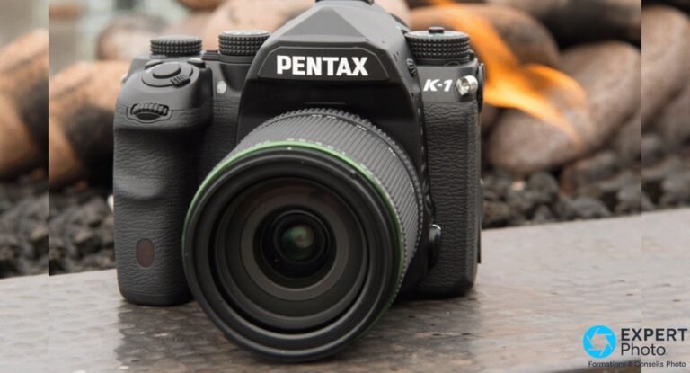 Pentax K-1 : ce que vaut encore ce reflex plein format sur le marché de l’occasion Pentax K-1 noir face avant 3/4, objectif zoom à bague verte monté, fond de galets orange flou