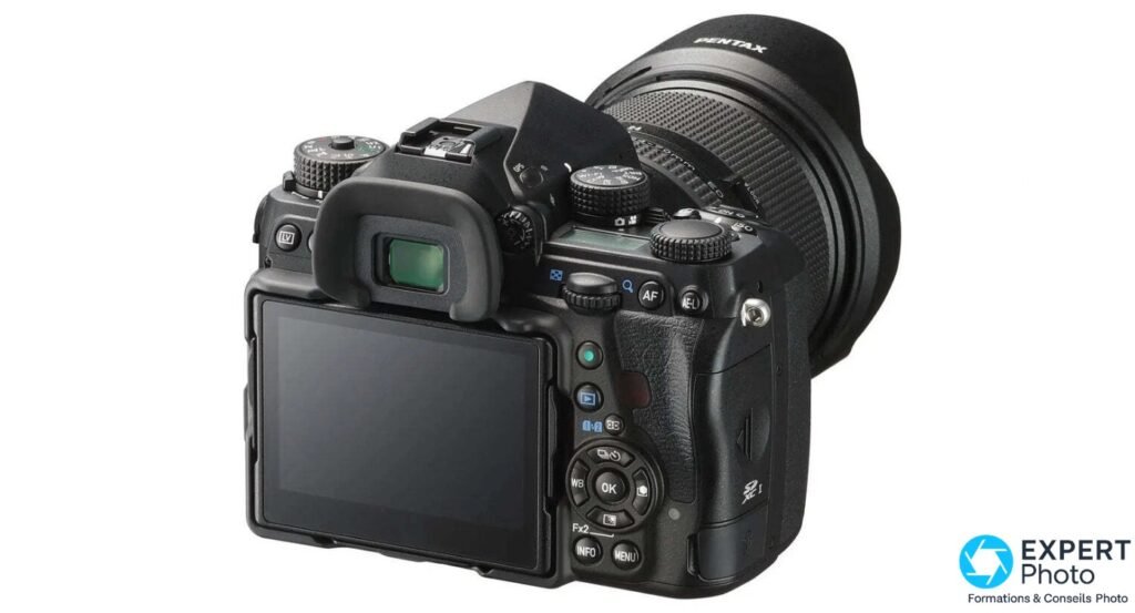  Pentax K-1 Mark II en 3/4 arrière, objectif zoom monté avec pare-soleil, écran LCD éteint, boutons arrière visibles