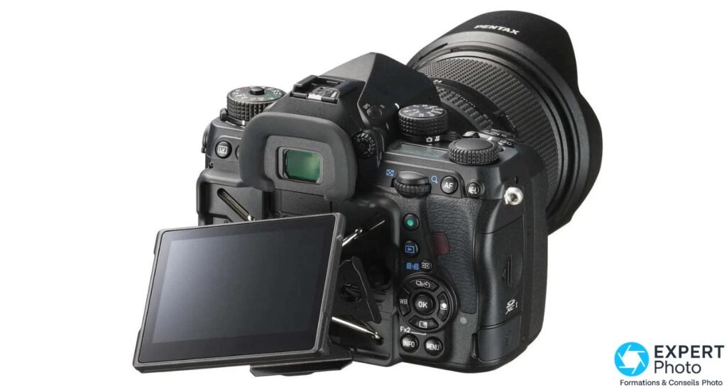 Pentax K-1 Mark II en 3/4 arrière, écran LCD orientable incliné vers le bas, objectif zoom avec pare-soleil