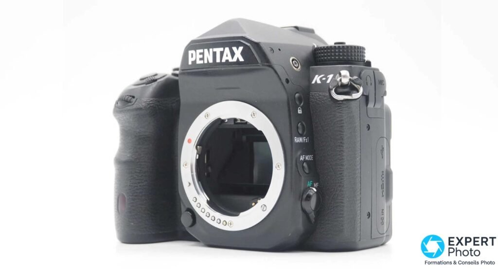 Pentax K-1 noir 3/4 avant gauche, boîtier nu monture visible, boutons RAW/Fx1 et AF MODE lisibles sur la tranche