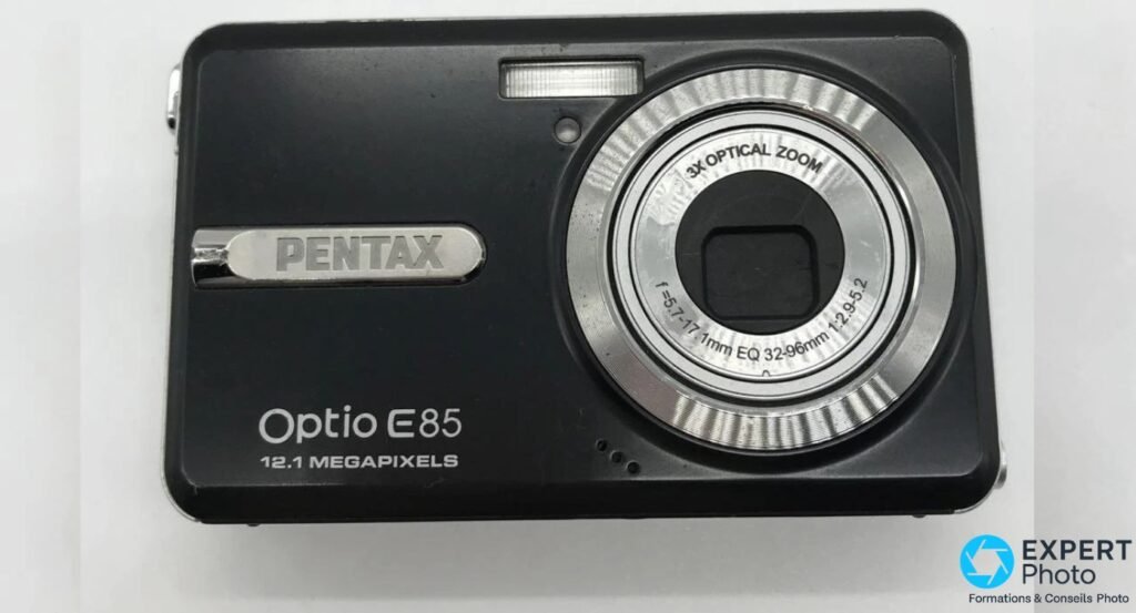 Pentax Optio E85 noir, face avant, zoom rétracté, badge PENTAX argenté, inscription 12.1 Megapixels, fond blanc
