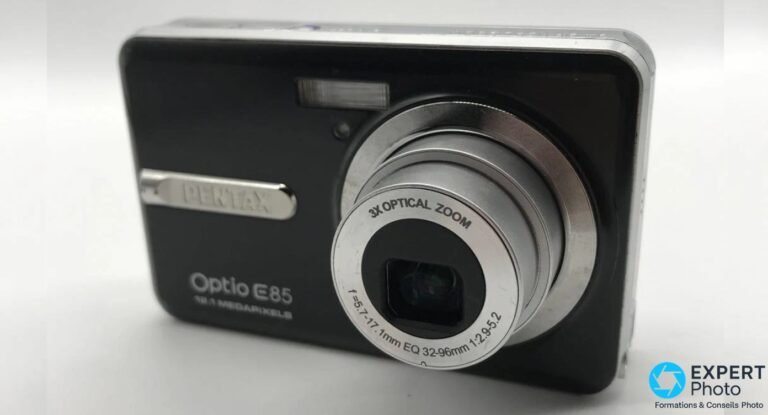 Pentax Optio E85 noir, angle 3/4 avant, zoom sorti, bague objectif argentée avec inscription 3X Optical Zoom, fond blanc
