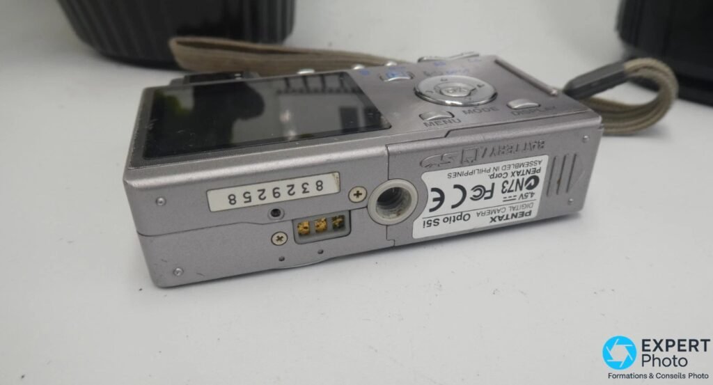 Dessous du Pentax Optio S5i : étiquette DIGITAL CAMERA, numéro de série, contacts dorés et trappe batterie. 
