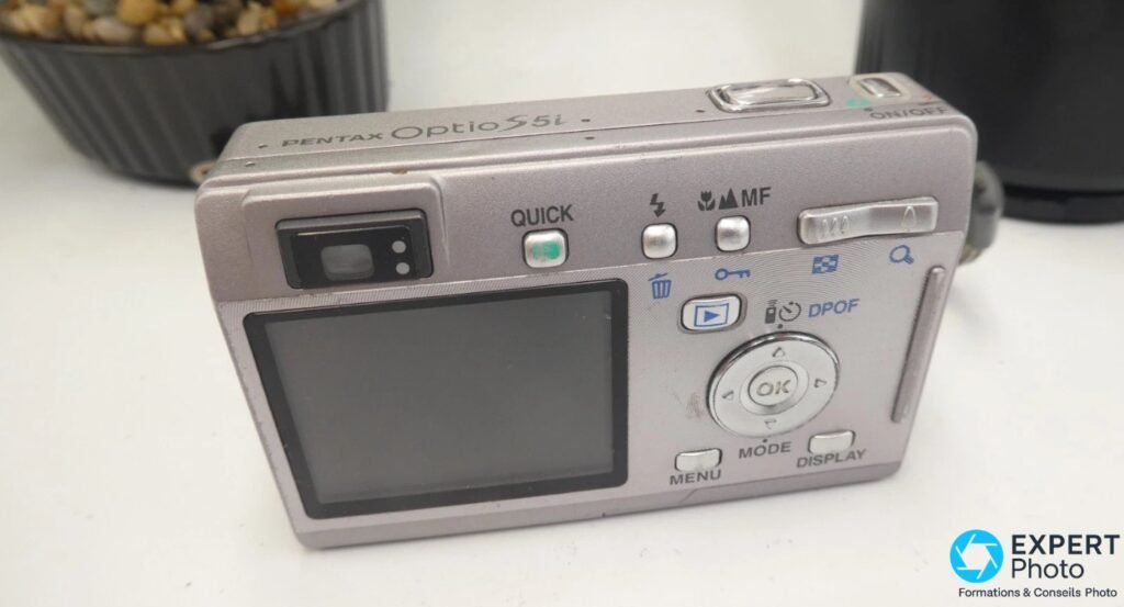 Pentax Optio S5i vu de dos : écran LCD éteint, molette OK, touches MENU MODE DISPLAY QUICK, inscription arrière.