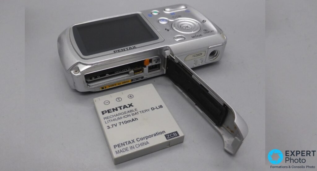 Pentax Optio WP, trappe batterie ouverte, batterie Pentax D-LI8 3.7V sortie, logement avec contacts dorés et joint visible