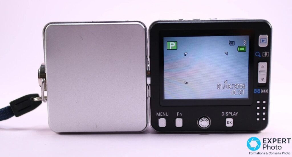 Dos du Pentax Optio X ouvert, écran LCD allumé en mode P avec date 01/09/2004, boutons MENU Fn DISPLAY OK visibles