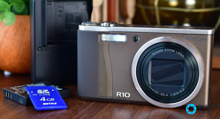 Ricoh R10 d’occasion : un compact CCD vintage pour un profil précis Ricoh R10 de face sur surface en bois avec carte SD 4 Go Buffalo et batterie lithium-ion au premier plan