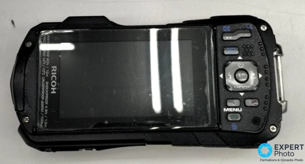 Ricoh WG-30W noir, face arrière, écran éteint rayé, inscriptions étanchéité 12 m et résistances moulées sur le boîtier