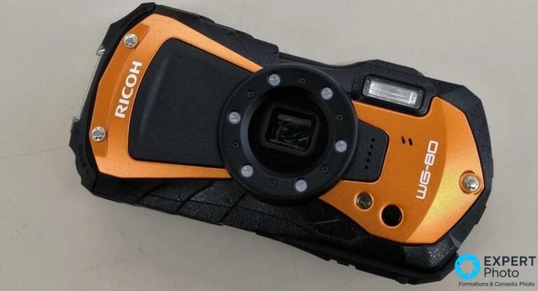 Ricoh WG-80 orange posé sur surface grise, vue de dessus en diagonale, gouttes d'eau sur le boîtier, anneau LED éteint
