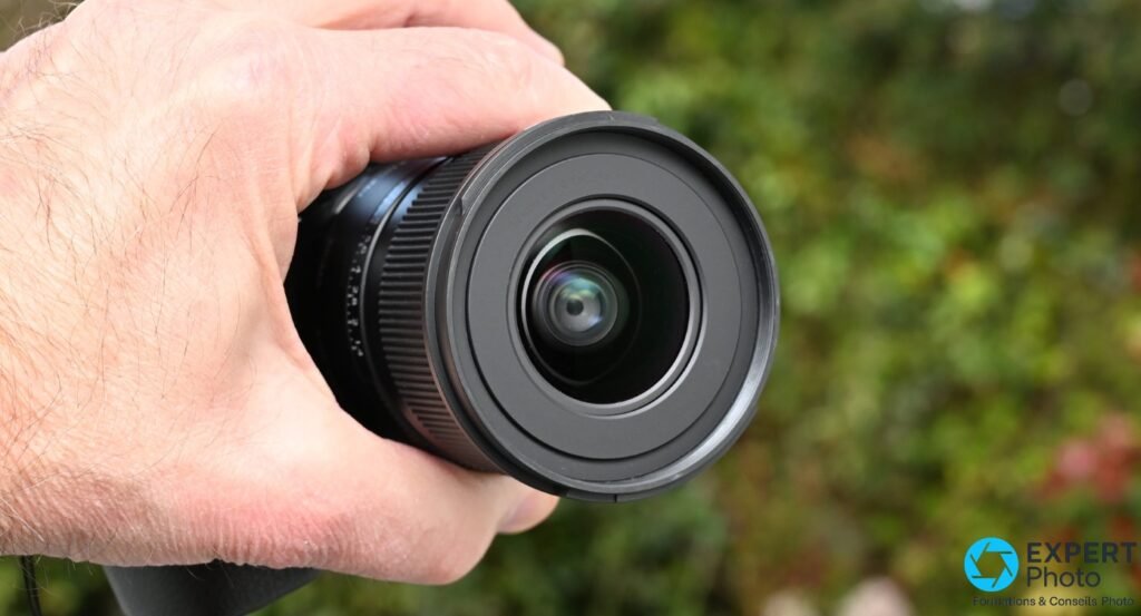 Sigma 12mm f/1.4 DC Contemporary, vue frontale de la lentille bombée avec reflets colorés, bague extérieure noire, tenu en main