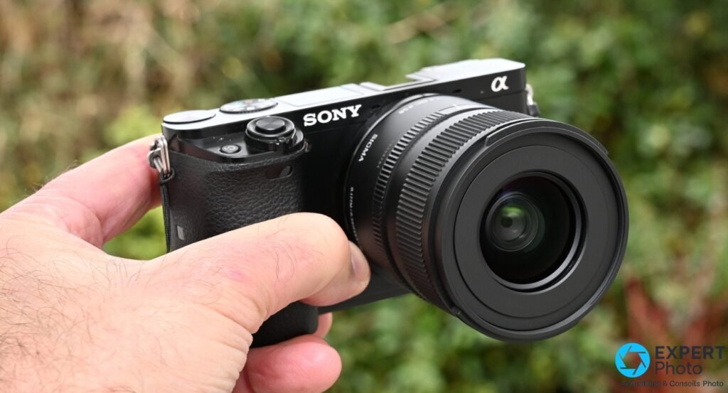 Sigma 15mm f/1.4 DC Contemporary en vue 3/4 avant sur Sony α : lentille frontale ronde, reflets verts, marquage SIGMA lisible