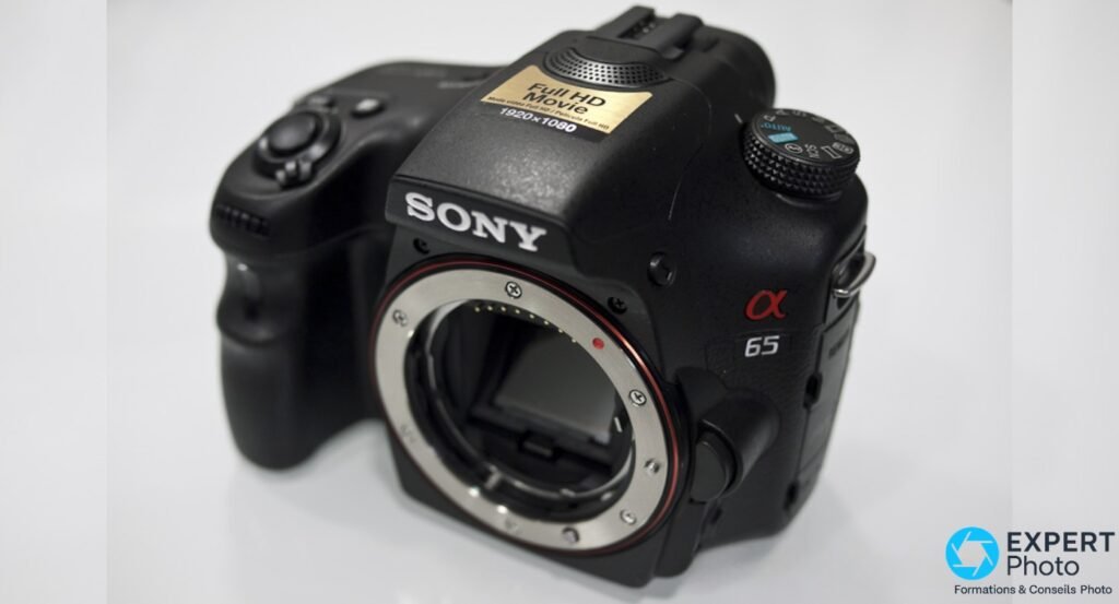 Sony Alpha 65 sans objectif sur fond blanc, monture A ouverte avec contacts électriques visibles et miroir semi-transparent apparent