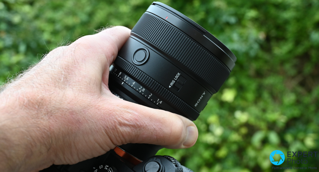 Sony FE 85mm f/1.4 GM II en main, graduation diaphragme 1.4 à 8, Iris Lock et SONY lisibles, boîtier Sony en arrière-plan.
